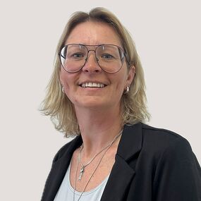 Das Portrait zeigt Yvonne Hartig. Sie hat schulterlange blonde Haare und eine große Brille. Sie lächelt freundlich.