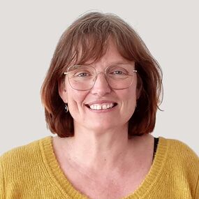 Das Portrait zeigt Martina Odorfer. Sie hat schulterlange braune Haare und einen Pony. Sie trägt eine Brille und grinst freundlich in die Kamera.