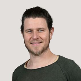 Das Portrait zeigt Ludwig Leonhardt. Er hat zusammengebundene dunkle Haare und einen Bart. Er lächelt in die Kamera.